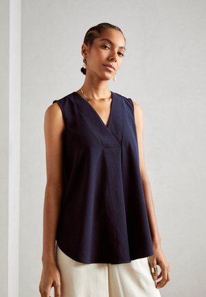 Dark navy sleeveless blouse with a v-neck, featuring a relaxed fit and soft texture. Paired with light-colored, wide-legged trousers.