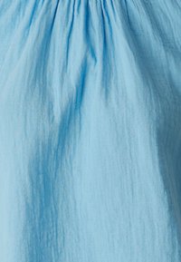 Tessuto di cotone azzurro chiaro con una texture stropicciata, arricciato sul colletto, creando morbide pieghe lungo tutto il design.