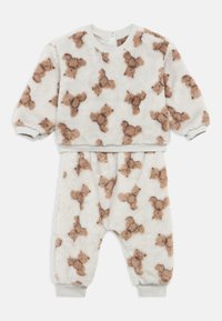 Costum moale alb pentru bebeluși, cu model de ursuleț maro, mâneci lungi și manșete elastice la mâneci și picioare.