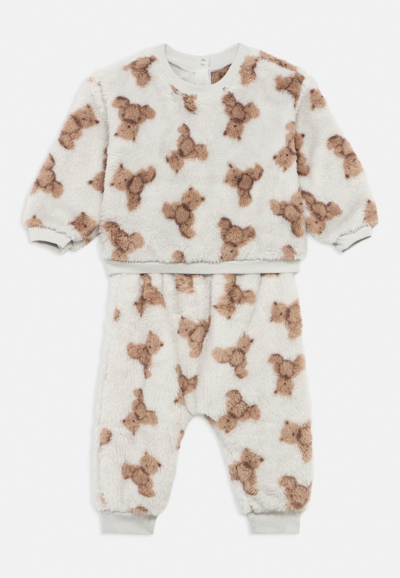 Costum moale alb pentru bebeluși, cu model de ursuleț maro, mâneci lungi și manșete elastice la mâneci și picioare.