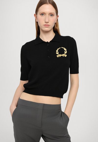 Cămașă polo neagră, scurtă, cu mâneci scurte, patru nasturi și un design brodat cu un coroană aurie pe partea stângă. Textură netedă, tricotată.