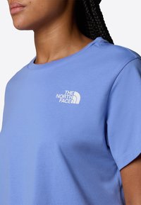 T-shirt azzurro chiaro realizzato in cotone morbido, con colletto rotondo e un logo bianco sul lato sinistro del petto. Maniche corte e texture liscia.