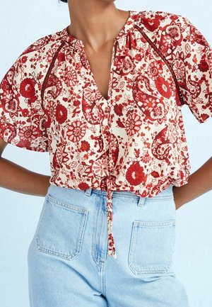 Rood blouse met bloemenpatroon en korte pofmouwen, gestrikt in de taille, gecombineerd met lichtblauwe spijkerbroek met hoge taille.