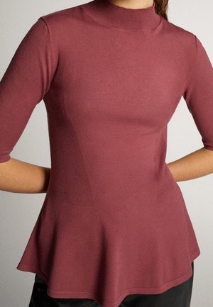 Fitted mauve top with mock neck, elbow-length sleeves, and flared hem worn with black pants.