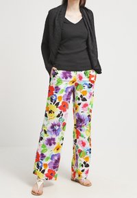 Floral wide-leg trousers with a white background, featuring multicolored flowers in purple, red, yellow, and green. Black top and sandals.