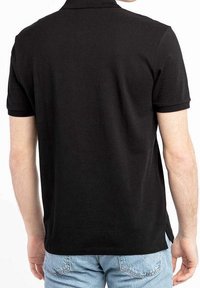 Chemise polo noire vue de dos, avec un col classique et des manches courtes, fabriquée en tissu lisse et léger.