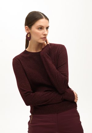 Pull bordeaux avec une finition texturée, manches longues et ourlet côtelé, assorti à de grandes boucles d'oreilles violettes avec un accent doré.