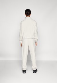 Chándal de felpa gris claro con cuello alto, puños elásticos y cinturilla, combinado con zapatos negros. Se muestra la vista posterior.