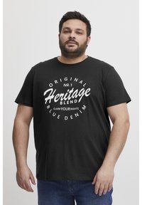 Juodas medvilnės marškinėliai su drąsiais baltais užrašais: "Original Heritage Blend" su akcentais ir apvaliu dizainu. Trumpomis rankovėmis ir apvalia iškirpte.