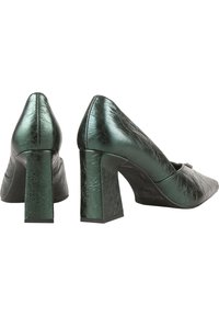 Paire de chaussures pour femmes en cuir vert métallisé à talons blocs, l'une montrant le talon arrière et l'autre le profil latéral sur fond blanc.