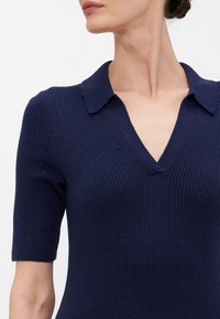 Polo en tricot côtelé navy avec un col en V et des manches courtes. Présente un col classique et une finition de tissu texturé.