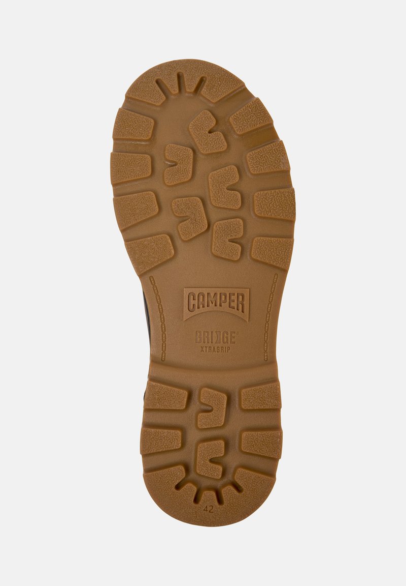 Semelle en caoutchouc brun avec un motif de traction texturé. Présente le logo "CAMPER" et l'inscription "BRIDGE XTRAGRIP", taille 42 indiquée.