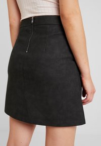 Minigonna in ecopelle nera con design aderente, zip centrale sul retro e dettagli di cucitura in alto lungo le cuciture.