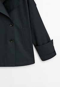 Czarna marynarka dwurzędowa z kołnierzem, z guzikami na zapięcie, boczną kieszenią i podwiniętymi mankietami. Gładka tekstura materiału.