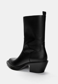 Cizmă ankle din piele neagră, cu o textură netedă, vârf rotund și toc masiv. Dispune de un sistem de prindere la spate și are un design minimalist.