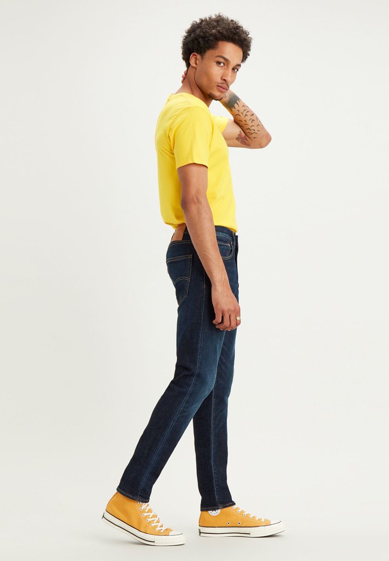 T-shirt jaune à manches courtes, jean bleu foncé et baskets jaunes. Les jeans possèdent des poches classiques et un design slim.