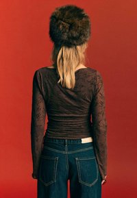 Smeđi top dugih rukava s cvjetnim uzorkom i nabranom teksturom, u kombinaciji s tamnoplavim trapericama koje imaju stražnje džepove, prikazano s leđa.