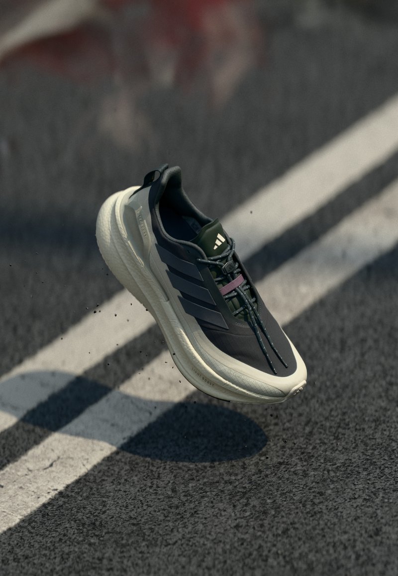 Μαύρο και ελιάς παπούτσι τρεξίματος με υφασμένο πάνω μέρος, ανοιχτόχρωμη σόλα και θηλιά έλξης, με τονικό λογότυπο τριών ρίγων και πράσινα κορδόνια.