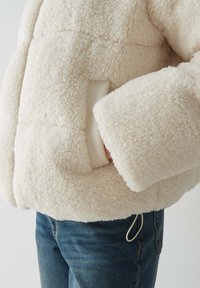 Giacca di colore crema, morbida e fluffosa, con un esterno texturizzato, dotata di una tasca nascosta, polsini aderenti e una silhouette rilassata.
