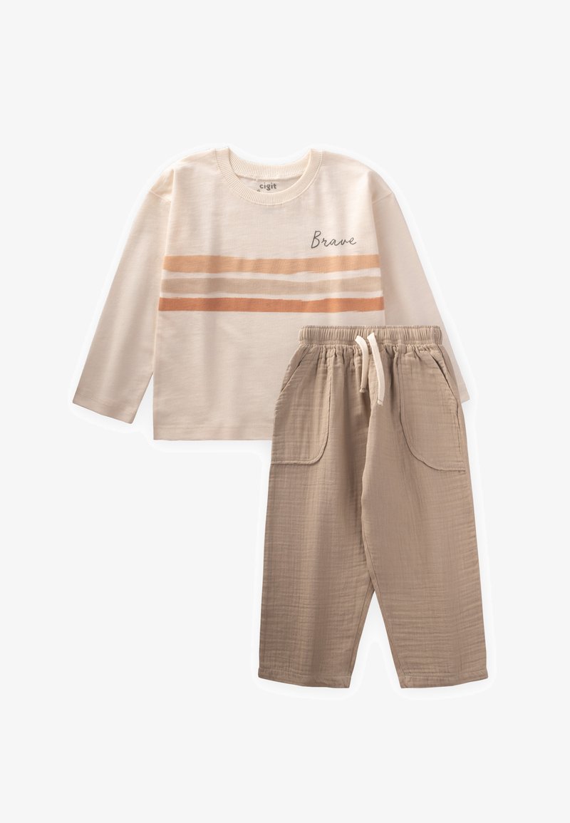 Maglietta crema a maniche lunghe con la scritta "Brave" e righe orizzontali; pantaloni beige a vita elastica con tasche laterali e tessuto strutturato.