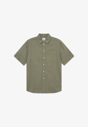 Chemise à manches courtes, de couleur olive, à boutons, fabriquée dans un tissu texturé. Elle possède une poche sur la poitrine et un logo sur le col.