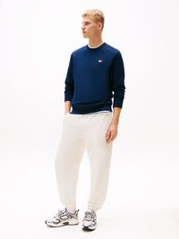 Sweatshirt azul-marinho com decote redondo e pequeno logo, combinado com calças de jogging brancas texturizadas e sapatilhas atléticas cinzas.