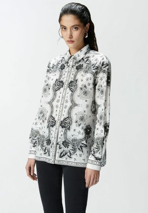 Camisa blanca de botón con patrones florales y geométricos en negro, de manga larga y con cuello clásico, fabricada en una tela ligera.