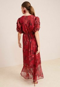 Raudona gėlių maxi suknelė su pūstomis rankovėmis, elastic juosmeniu ir permatomu audiniu. Pasiekia kulkšnis su tekės hemline.