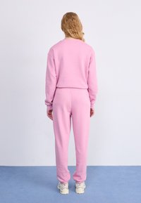 Sweatshirt en coton rose et joggings assortis. Caractéristiques : coupe décontractée, taille élastique et poignets côtelés. L'ensemble est porté avec des baskets blanches.