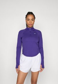 Lilla langermet zip-up topp med høy krage og hvit Nike-logo, sammen med hvite treningsshorts. Glatt stoff, slim fit-design.