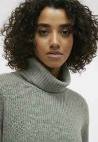 Svijetlozelena turtleneck pulover, pletena tekstura s rebrastim ovratnikom. Dizajniran za udoban kroj, s mekanim, ugodnim izgledom.