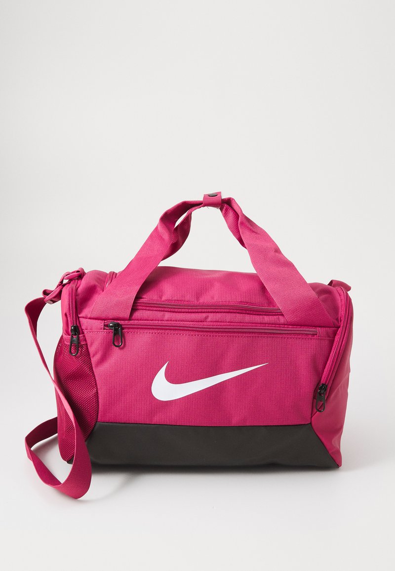 Ružová športová taška s čiernym dnom. Textilný materiál, zipsové priehradky, vrchné rukoväte a ramenný popruh. Biele logo Nike je výrazne zobrazené.