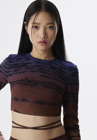 Langsleeve crop top in een gradient van paars naar bruin met zwarte abstracte tekstprints. Kenmerkt zich door een aansluitend ontwerp en gelaagde banddetails.