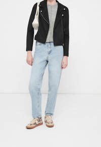 Giubbotto in suede nero da motociclista, maglietta grigia a coste, jeans a gamba dritta di lavaggio chiaro e sneakers con motivo e dettagli color sabbia. Borsa bianca.