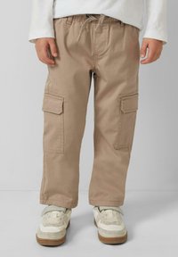 Beżowe spodnie cargo z bawełny, z dwiema kieszeniami bocznymi oraz elastycznym pasem ze sznurkiem. Połączone z białymi i beżowymi trampkami.