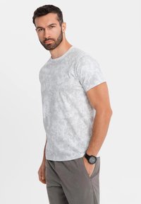 Šedé tričko s krátkým rukávem a kulatým výstřihem, kombinované se šedými kalhotami. Model má na zápěstí černé hodinky.