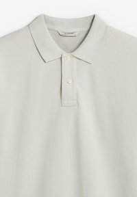 Camisa polo gris claro hecha de tela texturizada, con cuello, tapeta de tres botones y un sutil logo bordado en el pecho.