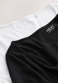Top sin mangas en blanco y negro con textura acanalada, con un escote cuadrado y etiqueta "NEXT" en el interior del cuello.