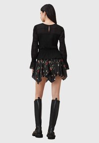 Blusa preta com franzido, de mangas longas e um recorte nas costas, combinada com uma saia rodada de estampa floral, usada com botas de couro pretas até ao joelho.