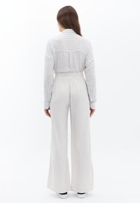 Lichtgrijs gestreept oversized shirt met een kraag en een elastische taille. Wijde pijpen, zachte textuur en volledige bedekking.