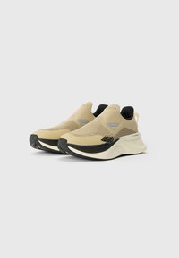 Beigā krāsā slip-on sporta apavi ar adītu augšdaļu, pelēkiem akcentiem, melnu papēža cilpu un biezām baltām starpzolēm. Strukturēts audums gaisa caurlaidībai.