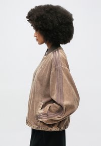 Καφέ μπουφάν bomber από κορντούρο με ριμπ υφή, που διαθέτει αντίθετο γιακά και κάθετες ρίγες στα μανίκια. Ελαστικά μανσέτα.