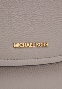 Lichtgrijs leer met een gestructureerde afwerking, voorzien van een gouden "MICHAEL KORS" logo en donkere stiksels langs de randen.