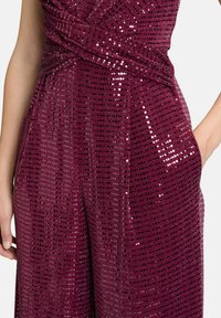 Combinaison bordeaux avec une finition texturée et pailletée. Présente un design enveloppant, des jambes larges et des poches latérales discrètes.