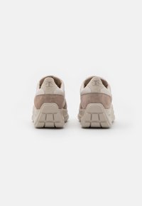 Beige och vita sneakers med mocka och lädermaterial. Tjocka, strukturerade sulor med framträdande mönster. Logotyp präglad på hälen.