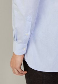 Lichtblau gestreept shirt met knoopmanchetten, met een gladde textuur en een gebogen zoom, in combinatie met donkere broeken.