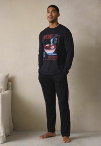 Zwart T-shirt met lange mouwen en een grafische print van een kom ramen. Gecombineerd met zwarte broek met een ontspannen pasvorm en zachte stof.