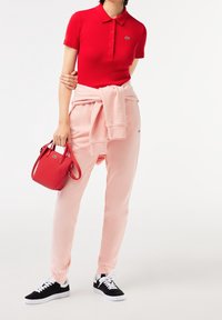 Polo rojo de manga corta con tres botones, pantalones de chándal rosas atados en la cintura, zapatillas negras y un pequeño bolso rojo.