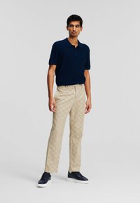Navy knit polo, beige patterned trousers with logo detail, white soles on dark shoes; modern fit and texture contrast throughout.