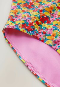 Stoff mit floralem Muster in lebhaften Farben (rot, gelb, blau, pink). Glatte rosa Innenseite mit gesticktem Rand; Badeanzug-Design mit Highlights.